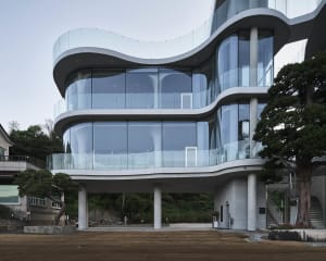 A modern building with a glass exterior, featuring a minimalist and functional design with a focus on open spaces and natural light, set against a backdrop of a tree and a subtle blend of rendered and photographic elements