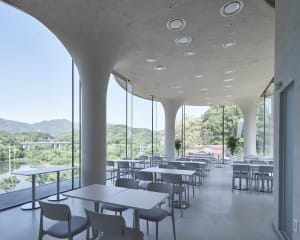 Modern restaurant interior with multiple tables, booths, and chairs, featuring clean lines, minimal decoration, and warm lighting