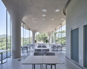 A spacious restaurant with concrete walls, dim lighting, and numerous dining tables and chairs