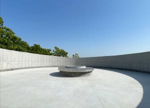 A serene outdoor space with a circular stone structure surrounded by a cement wall and trees in the background