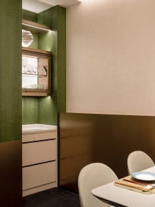 A kitchen with green walls, white cabinets, and a dining table in the background, featuring wine glasses and scattered cups