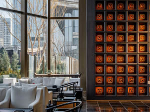 A modern dining space with a lit tile wall, comfortable seating, and potted plants, conveying a stylish and inviting atmosphere