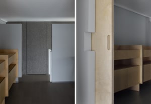 A modern bedroom with wooden floors and walls, featuring two beds and a chair, with a focus on functionality and aesthetics