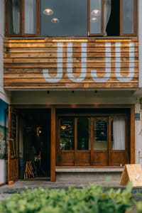 Modern building with a wooden facade, a large sign reading JUJI in white letters, and a doorway with a staircase