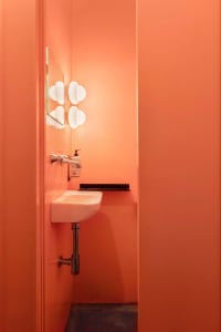 A well-lit bathroom with a wall-mounted sink, white basin, and two mirrors, painted walls in a warm hue