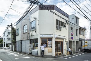 A busy coffee shop with a brick exterior, white interior, and customers seated at tables and standing outside
