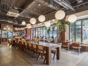 Casual dining area with wooden tables and chairs, people enjoying meals, warm ambiance from hanging lights