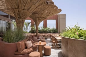 A restaurant patio area with a large straw or reed umbrella providing shade for dining tables and comfortable seating for guests