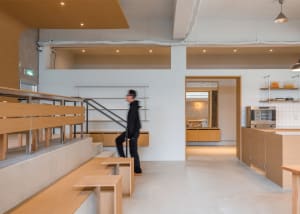 Open commercial space with wooden floors, white walls, and benches, featuring a man walking through the area