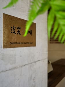 A cozy coffee shop interior with a sign featuring Chinese characters, two potted plants, and a dining table in the background