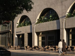 A building with an archway leading to a courtyard, featuring variously sized chairs in a welcoming outdoor-indoor space