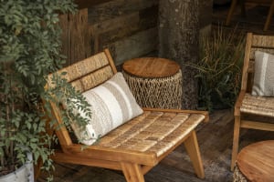 A wooden bench with a woven design, situated in front of a tree trunk, with two pillows and a natural atmosphere