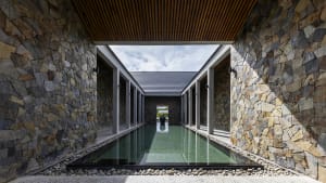 A well-lit indoor pool area with two pools, surrounded by stone walls and featuring a modern and luxurious interior design