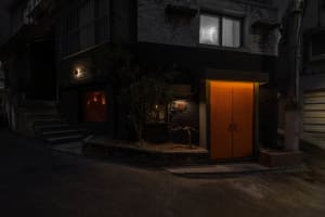 A black house with an orange door and two windows on either side, suggesting a warm and inviting living space