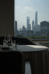 A rooftop dining space with a set table, wine glasses, and a city view from a high vantage point