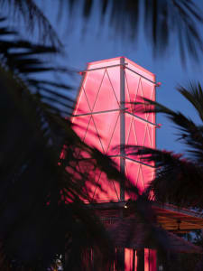 A modern building with a pink structure on its side, set against a tropical backdrop of palm trees and a clean, minimalist design