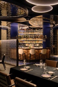 A cozy bar area with a large mirror behind the counter, surrounded by chairs and bottles on display