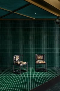 Two chairs placed at an angle in front of a green wall, creating a sense of depth and balance in a calm and inviting space