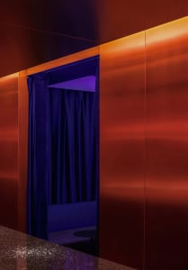 A small, dark room with a red wall and a blue curtain covering a doorway, with no other objects or details visible
