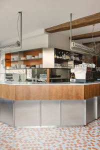 A casual dining bar with a wooden counter, bottles, cups, bowls, and wine glasses, set in a warm and inviting atmosphere