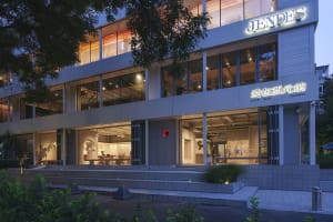 A modern building with white walls, glass windows, and potted plants, featuring a spacious and contemporary design with scattered chairs