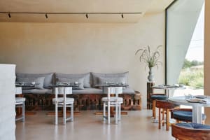 A modern restaurant with grey couches and stone walls, featuring several dining tables and chairs in a dimly lit space with a cozy ambiance