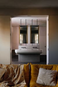Bathroom with a marble countertop, two faucets, two mirrors, and a wooden floor, well-lit