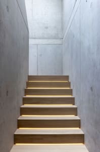 A well-lit stairwell in a building with concrete walls and steps, illuminated by lights on each step