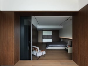 Cozy bedroom with wooden floors and walls, featuring two beds and a chair, with a warm and inviting atmosphere