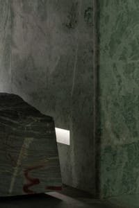 A dimly lit interior space with a large stone wall, creating a moody atmosphere