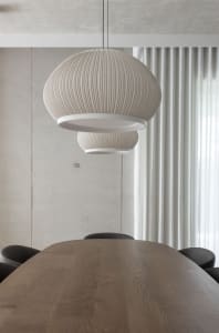 A modern dining space with a wooden table surrounded by chairs, lit by hanging lamps and providing a comfortable seating arrangement