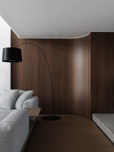 Cozy living area with a couch, chair, and lamp, surrounded by wooden panel walls and illuminated by a prominent lamp