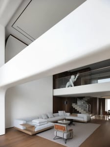 Open modern living area with a white couch, a sculpture on the wall, two chairs, a dining table, and a potted plant, creating a clean and inviting atmosphere
