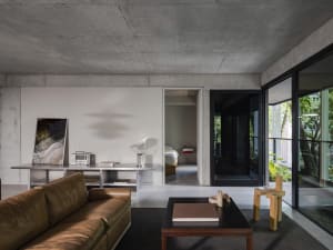 A modern living room with a large couch, chair, dining table, two beds, bookshelf, and clock, set against a clean and minimalist backdrop of white walls and grey flooring