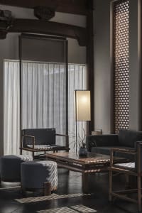 A modern living area with a couch, chair, coffee table, and lamp, surrounded by potted plants and a cozy atmosphere