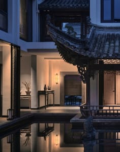 A serene Asian-style house with a large roof, wooden walls, and a courtyard featuring a pond, chairs, and a tranquil atmosphere