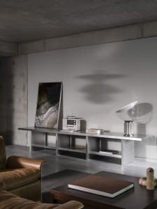 Modern living room with a couch, chair, and dining table, featuring grey walls and a concrete floor, with various pieces of furniture and decorative items