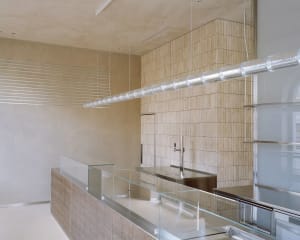 A well-lit kitchen area in a restaurant with a modern design, featuring a sink, refrigerator, microwave, and natural/artificial lighting