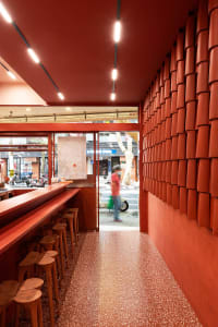 A cozy bar area with a counter, stools, and dining tables, featuring orange walls and warm lighting, with a motorcycle parked outside