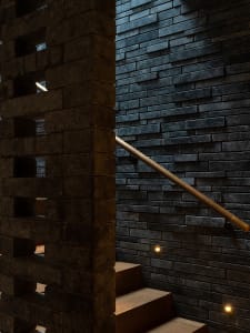 A classic interior stairwell with a brick wall, wooden railing, and stone stairs, evoking a sense of history and timelessness