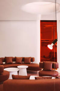 A modern living area with brown leather chairs and couches arranged around a coffee table, surrounded by red walls and white accents