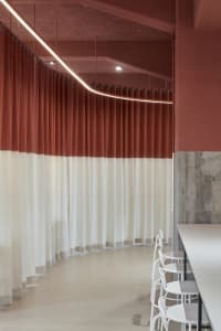 A minimalist room with red walls, white curtains, and two chairs, creating a calm and inviting atmosphere