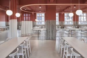 A modern restaurant interior with red walls, multiple tables, chairs, and natural light from windows