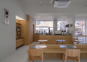 A modern cafe with a large dining area featuring white walls, several tables, and chairs, creating a bright and airy atmosphere
