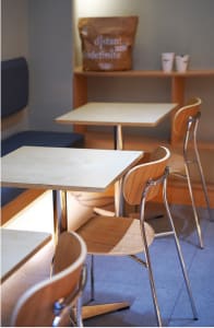 A restaurant interior with multiple dining tables, chairs, and benches, featuring wood elements and warm lighting