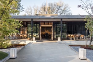 Modern restaurant with glass walls, wood accents, and natural light, featuring dining tables and chairs in a comfortable and inviting atmosphere