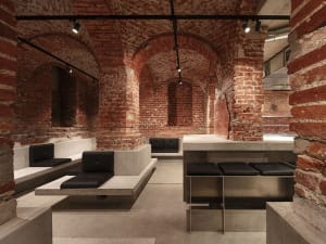 Dimly lit restaurant interior with brick walls, stone flooring, and black cushioned benches