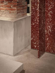A warm and inviting room with a red marble wall, stone columns, and a brick-patterned fireplace