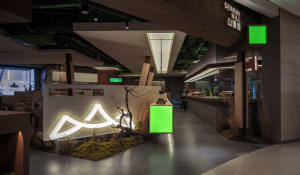 A lively cafe with a large green display box, people standing and sitting throughout the space, and a mix of industrial and decorative elements
