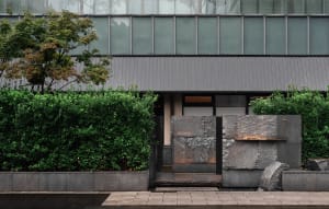 Modern building with a large stone wall and doorway, set against a natural backdrop of trees